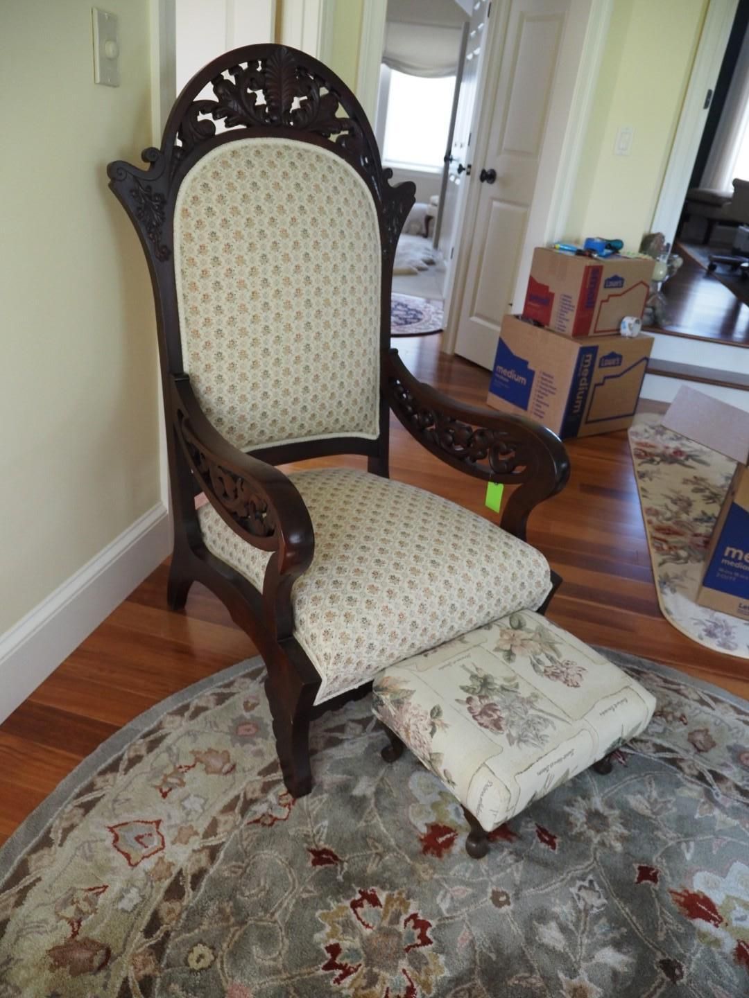 Dark wooden armchair with carved details and floral patterned upholstery, with matching footstool on a round rug.