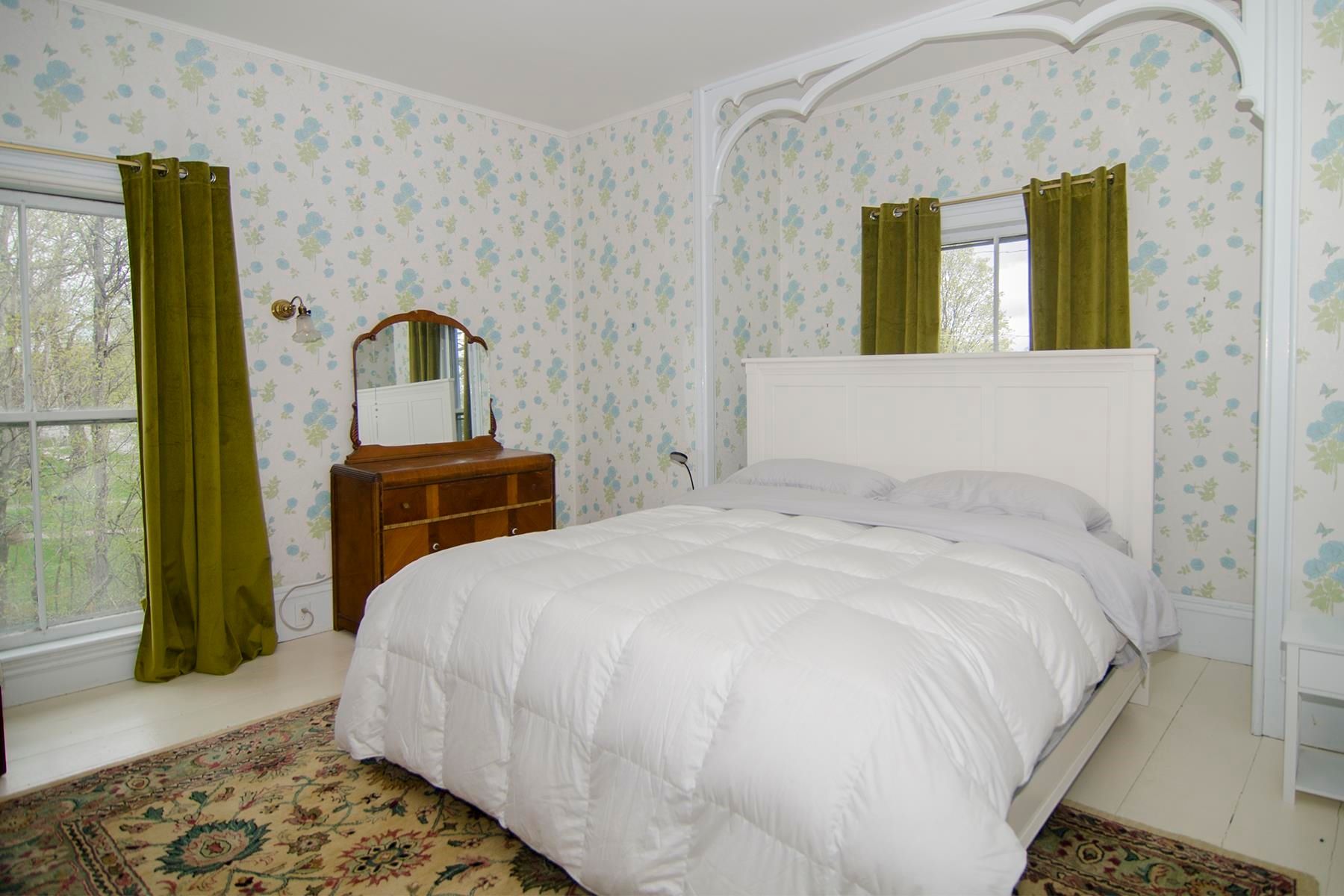 Bedroom with white bed, floral wallpaper, green curtains, and a wooden dresser.