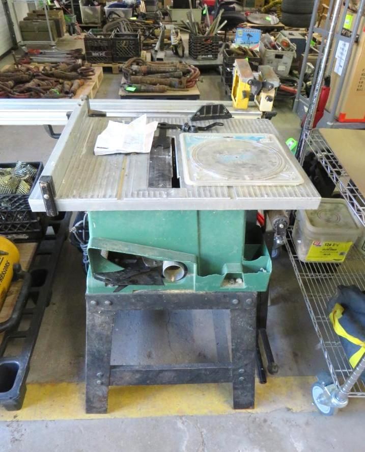 Green table saw on a black wooden stand, in a workshop setting.