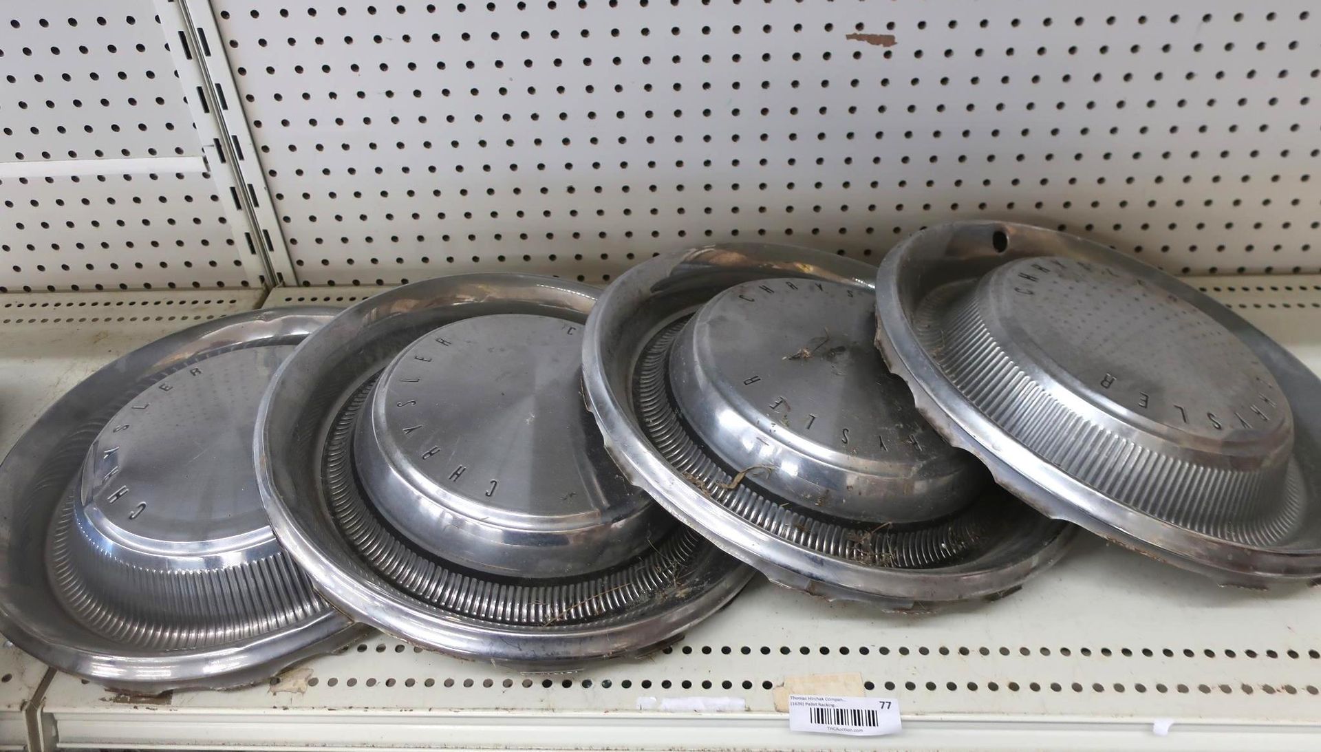 Four silver hubcaps on a shelf, displayed against a pegboard backdrop.