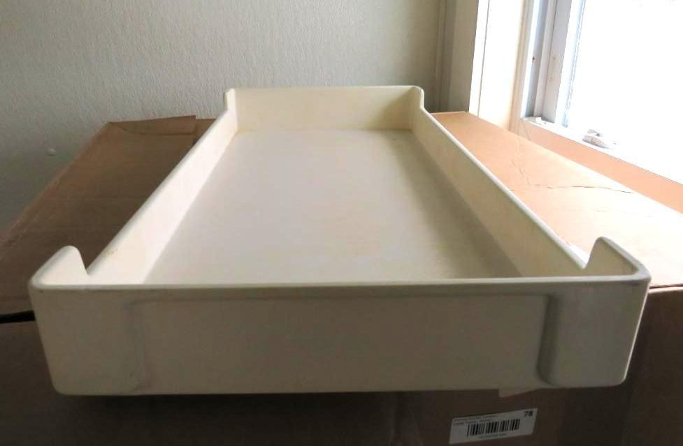 Off-white plastic baby changing table with raised edges, sitting on a box near a window.