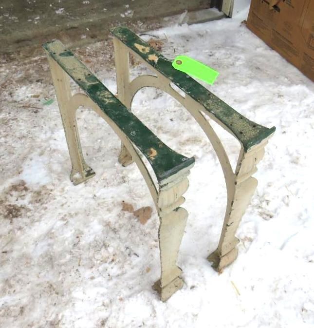 Two cast iron table legs, arched, with green and off-white paint, on snow.