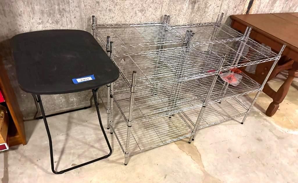 Black folding stool beside a metal shelving unit and wooden table in a room with a concrete wall.