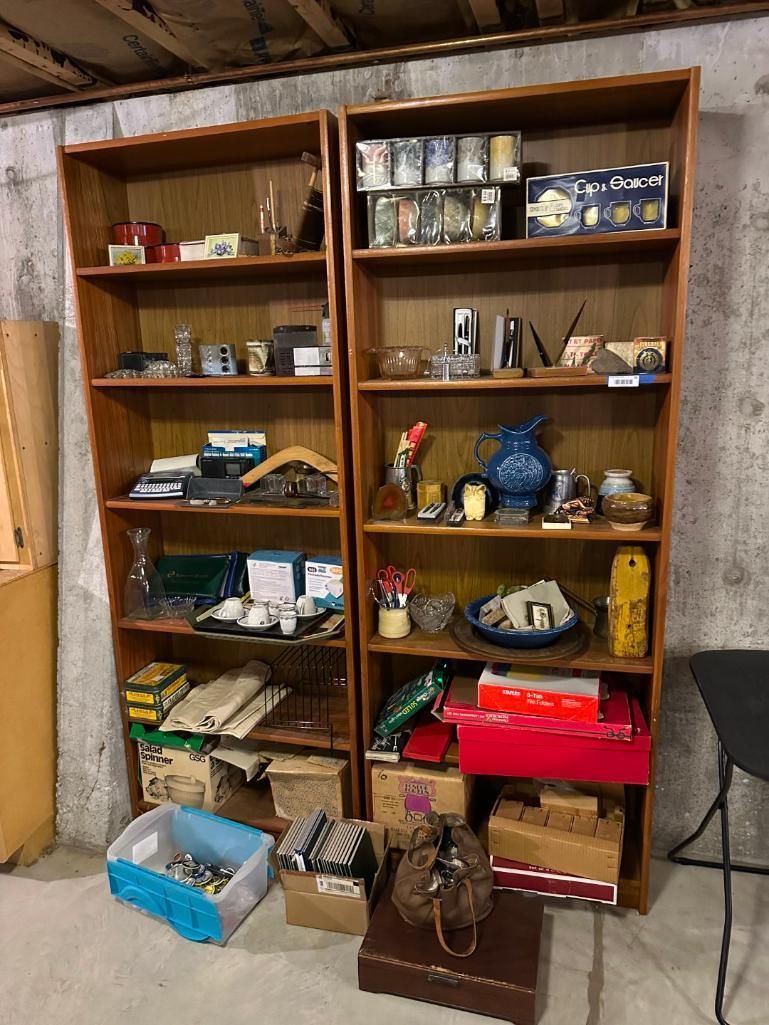 Two tall wooden bookshelves filled with various objects, set against a concrete wall.