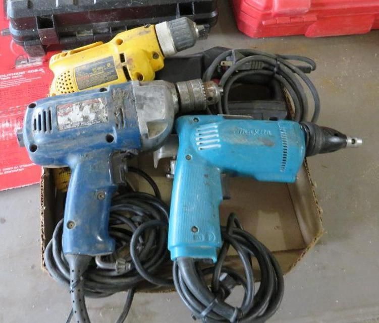 Three power drills: yellow, blue, and teal, with black cords in a cardboard box.
