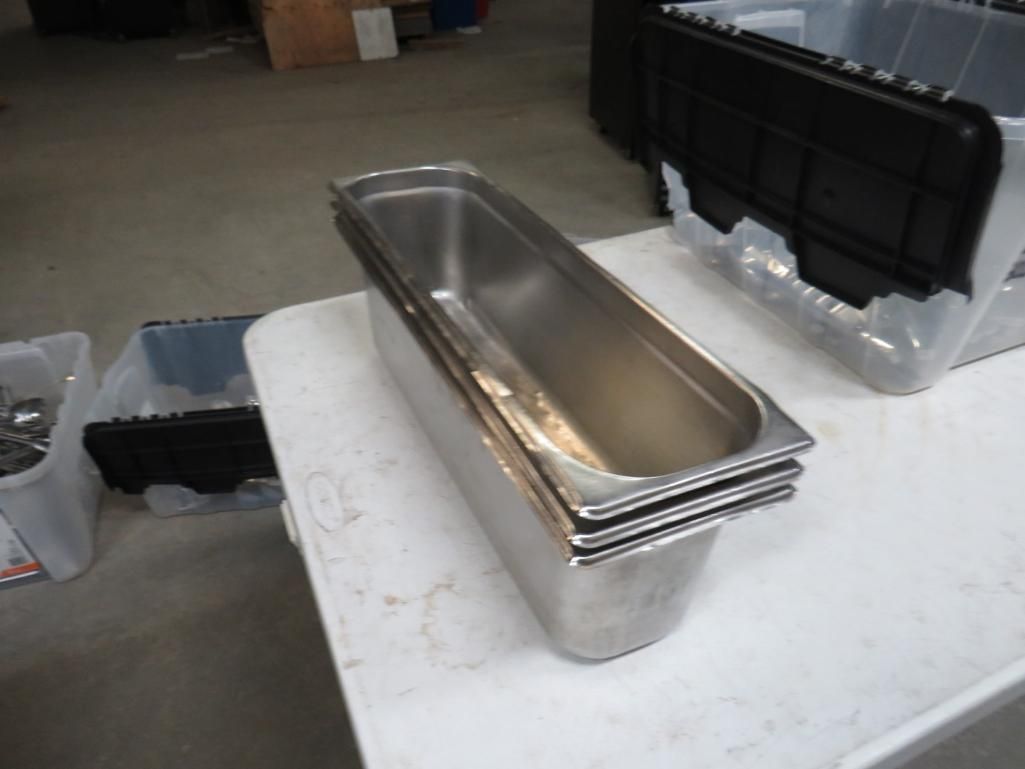 Stack of stainless steel food storage pans on a white table, with other bins nearby.