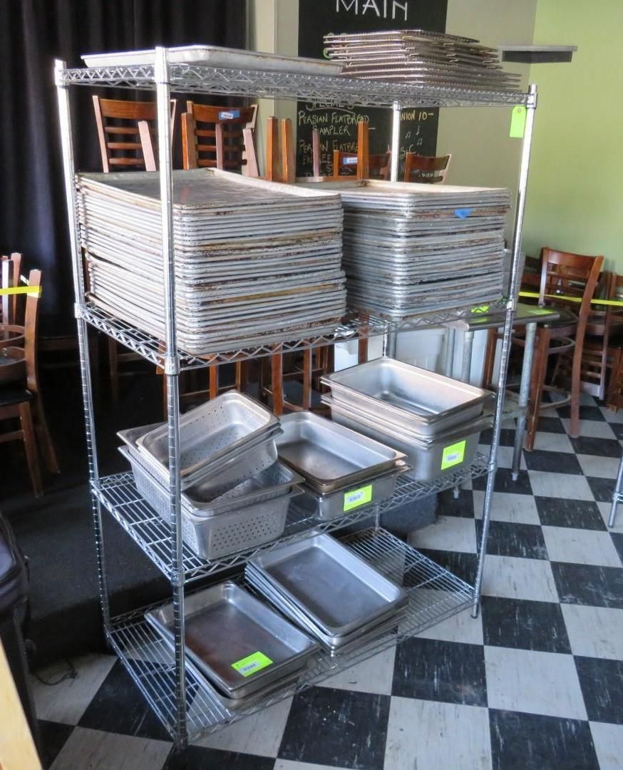 Metal shelving unit stacked with various stainless steel food pans and trays, likely in a restaurant.