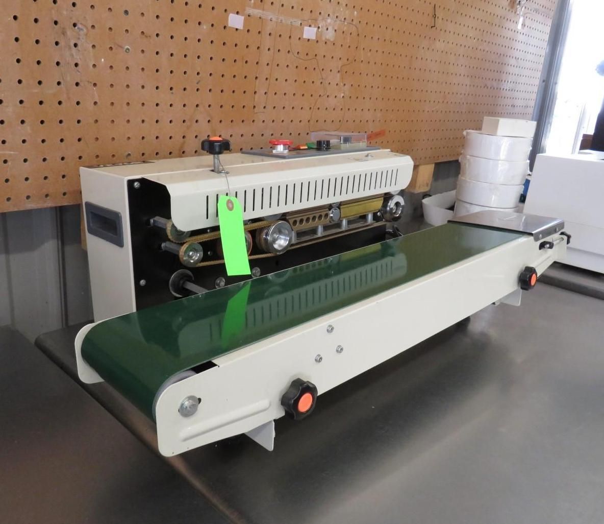 White and green automated bag sealing machine with conveyor belt, indoors.