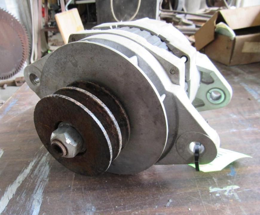 Close-up of a silver alternator with a three-groove pulley, sitting on a work surface.