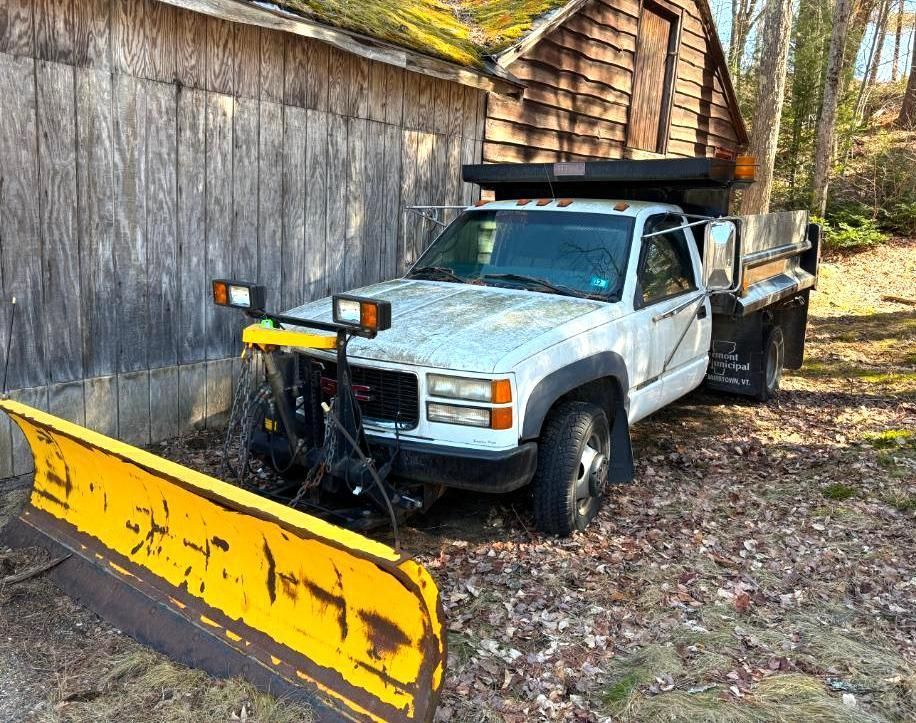 White pickup truck with yellow snowplow parked next to a wooden building.