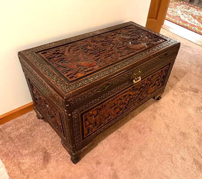 Dark brown, ornate wooden chest with detailed carvings, resting on a brown carpet.