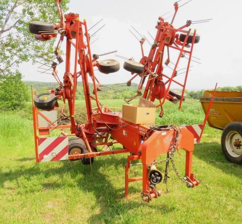 Orange hay rake in a grassy field, with tires mounted and a cardboard box.