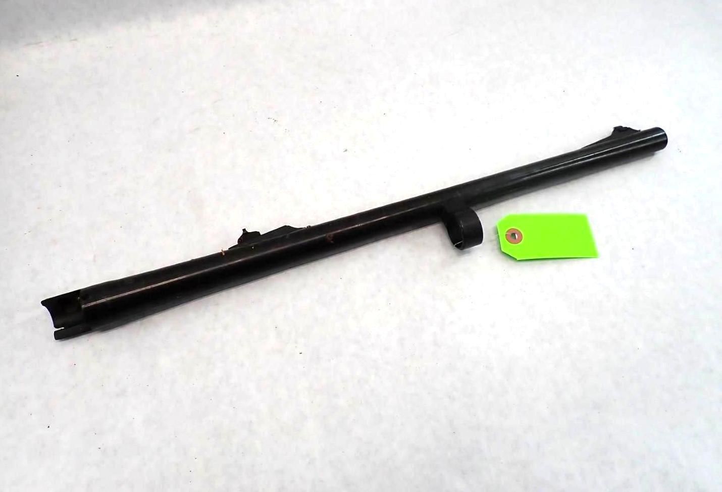 Black firearm barrel with a green tag on a white surface.