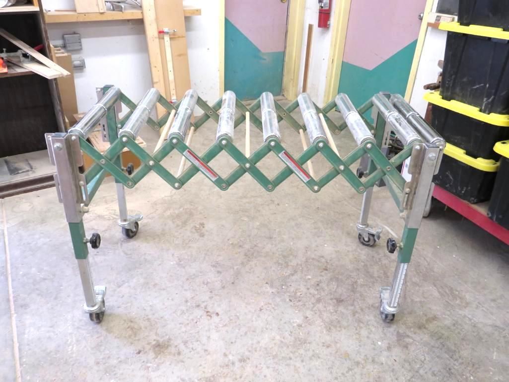 Expandable roller conveyor table, green and silver, on wheels, in a workshop.
