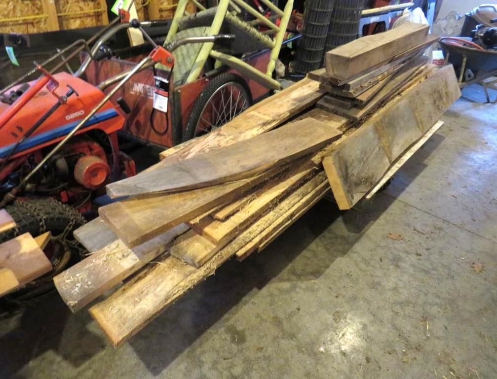 Pile of wooden planks in a garage, with a lawnmower in the background.