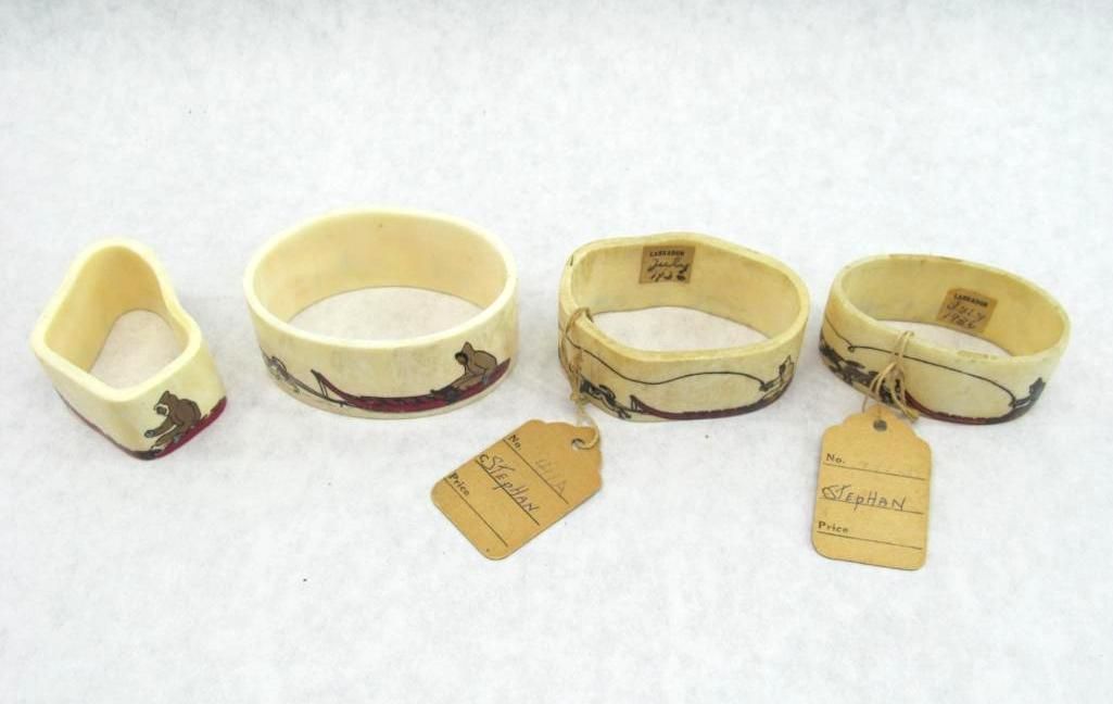 Four off-white napkin rings with embroidery and tags, on a white surface.