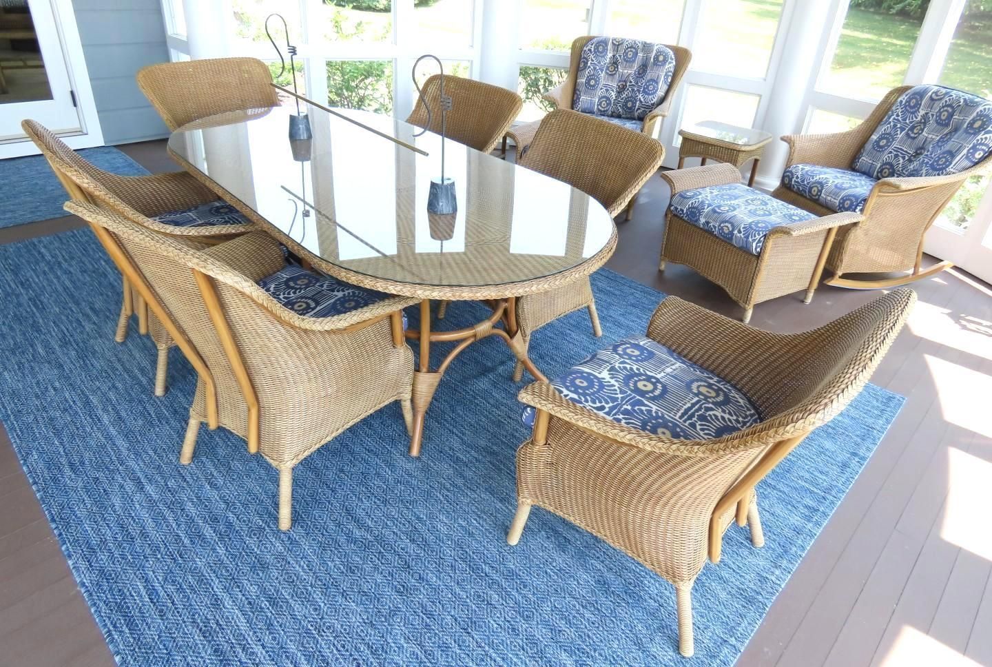 Wicker dining set with blue cushions and a glass-topped table on a blue rug in a sunroom.