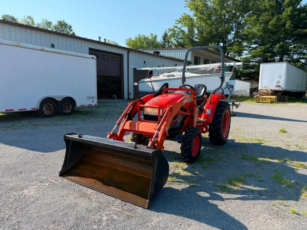Red tractor with front loader parked on gravel outside a white industrial building