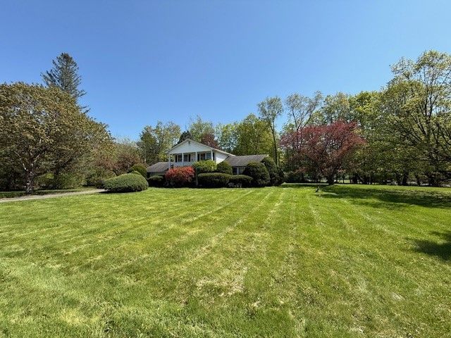 Ranch-style house with manicured lawn, surrounded by trees under a clear blue sky.