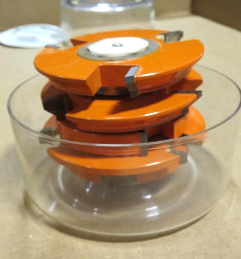 Four orange router bits stacked inside a clear plastic bowl.