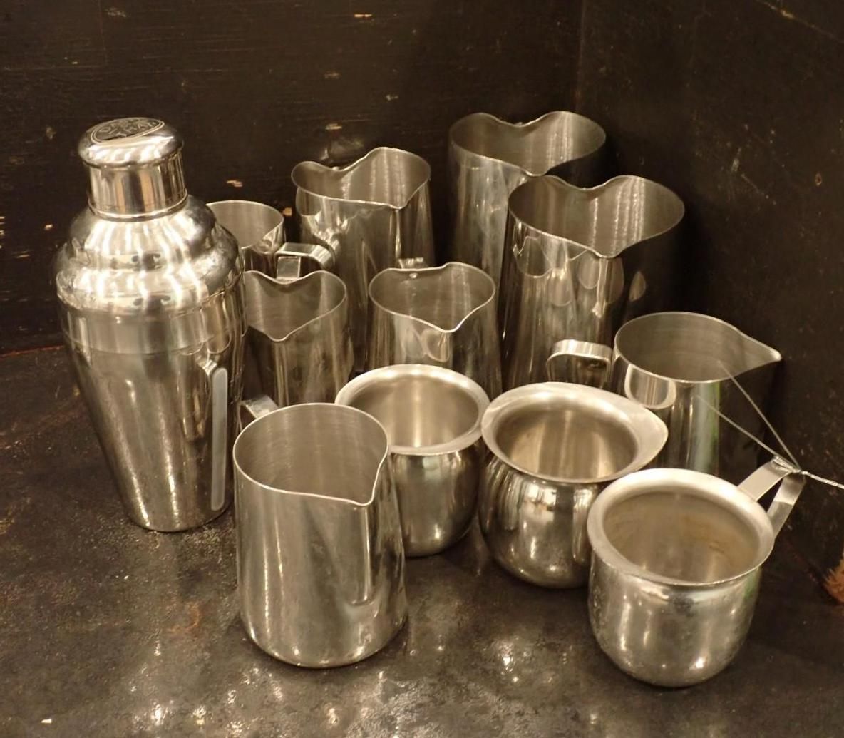 Various stainless steel pitchers and a shaker on a dark surface.