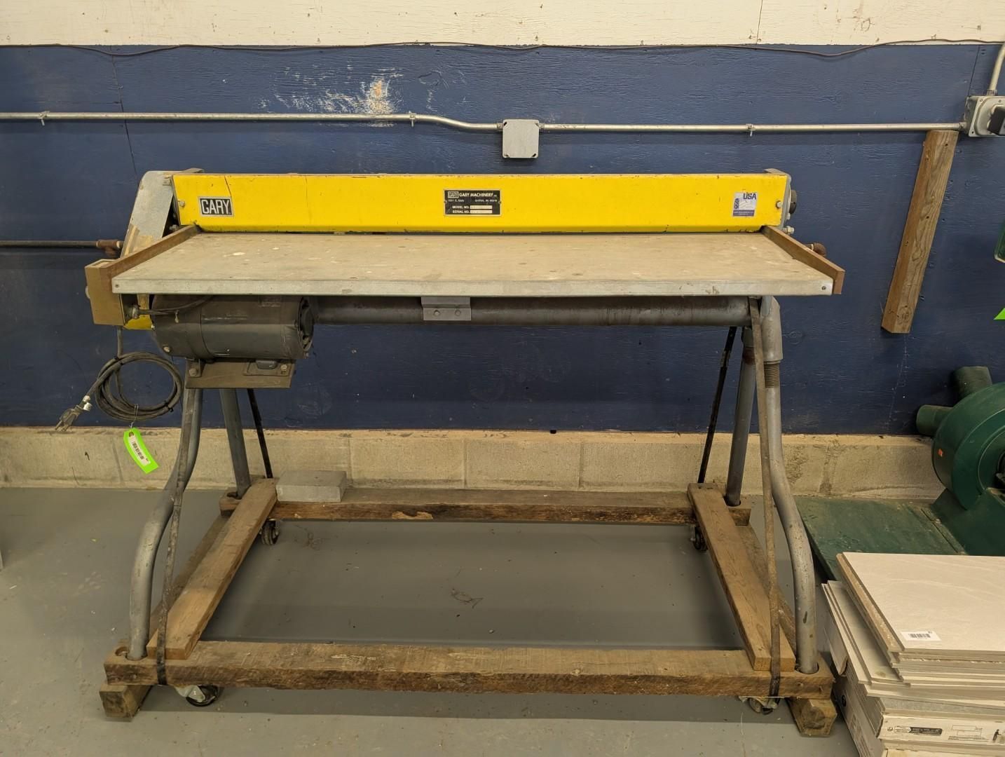 Yellow paper cutter machine on a wheeled metal stand in a workshop.