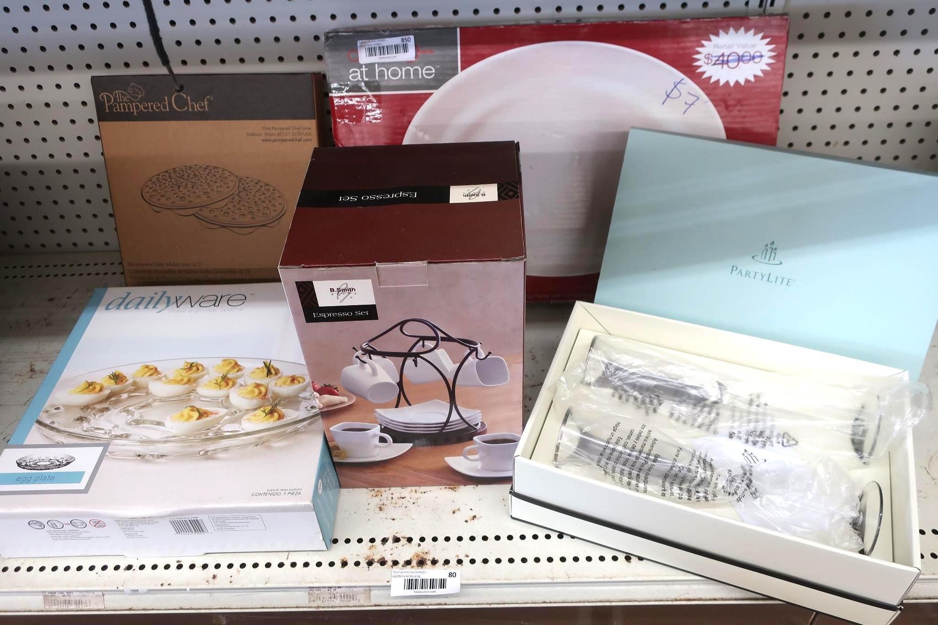 Boxes of tableware on a shelf: plates, serving dishes, teacups, and silverware.