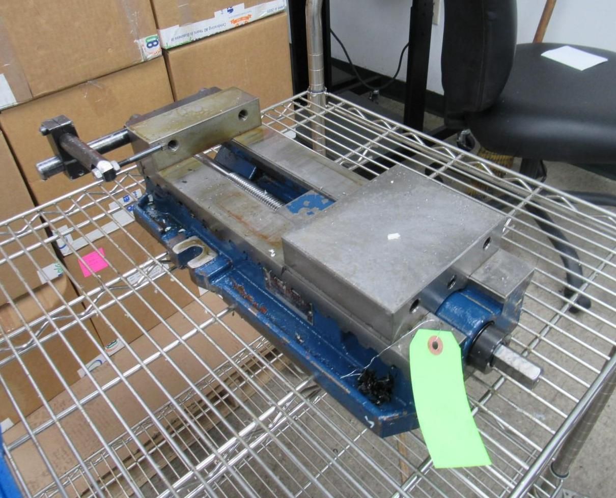 Blue and gray milling machine vise on a wire rack with a green tag attached.
