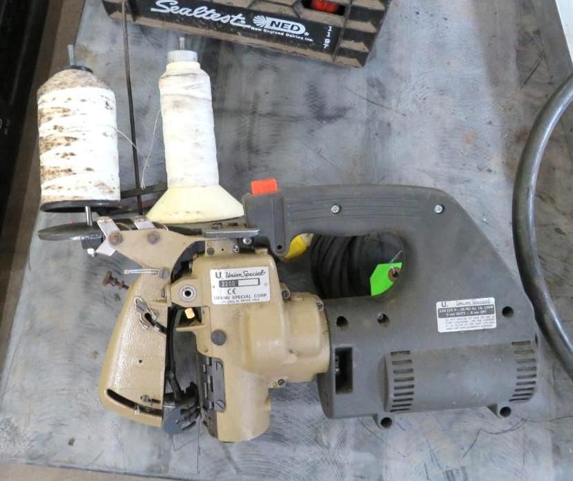 A beige portable sewing machine with two white thread spools attached, on a gray surface.