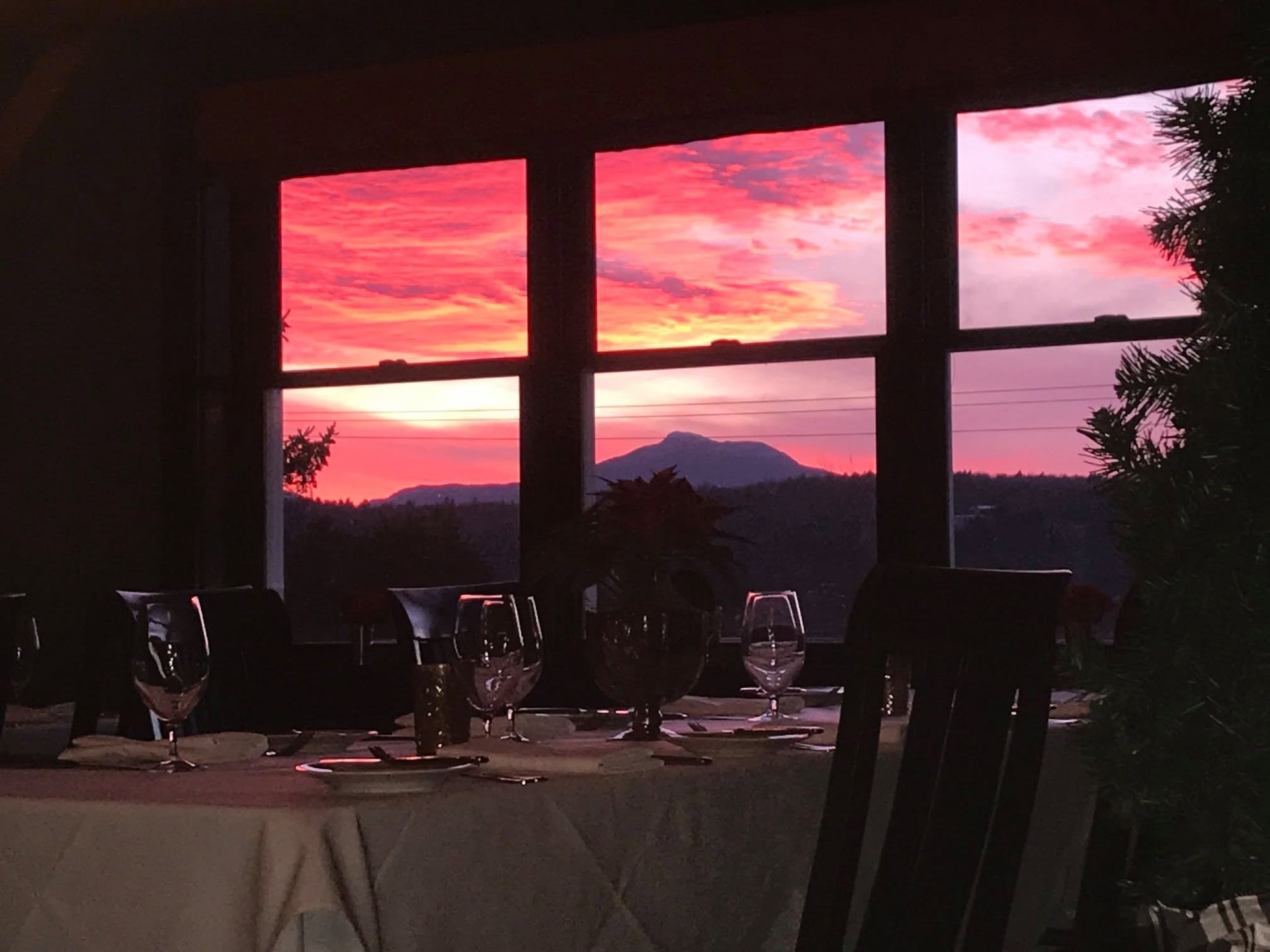 Dining table by a window at sunset with pink clouds and mountain silhouettes.