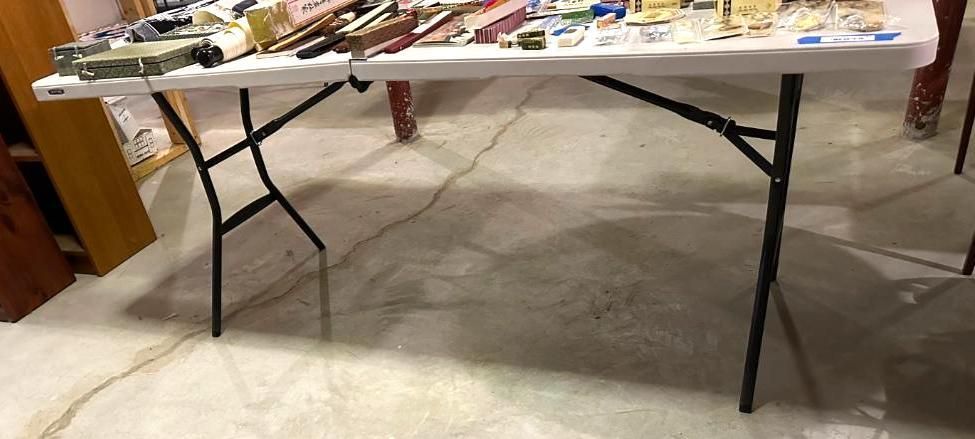 A white folding table with black legs, laden with items, sits on a concrete floor.