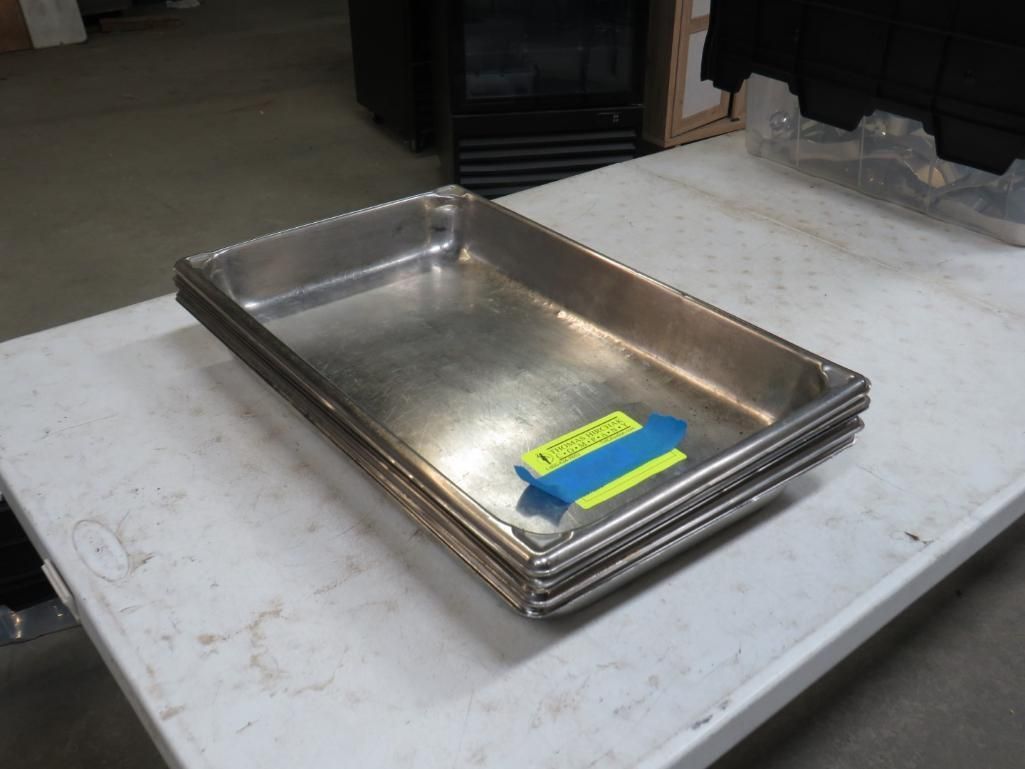 Stack of rectangular stainless steel food pans on a white table with a blue and yellow tag.