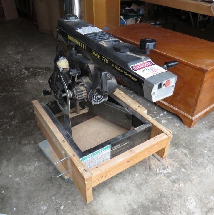 Radial arm saw on a wooden stand in a workshop setting.