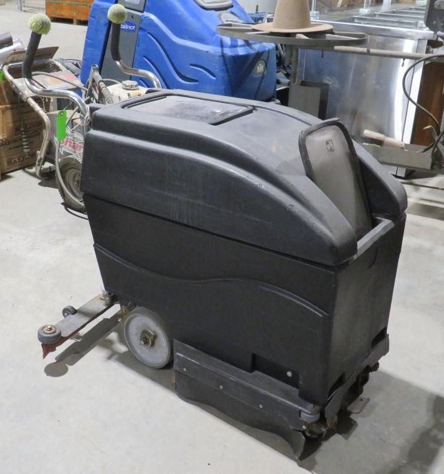 A large, black floor cleaning machine with two wheels, in a warehouse setting.