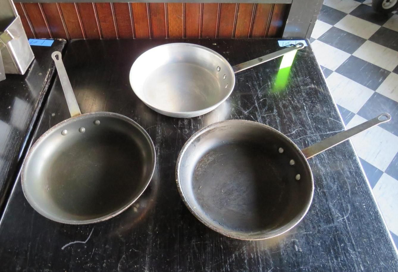 Three stainless steel frying pans on a black surface.