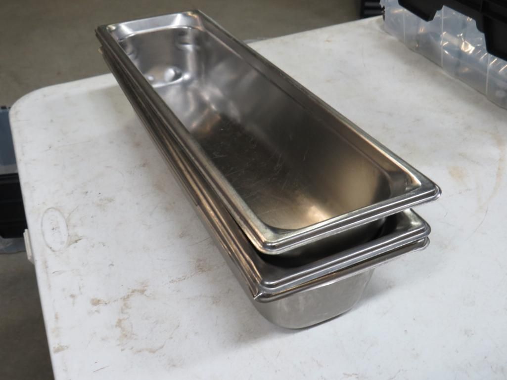 Stack of stainless steel food pans on a white table.