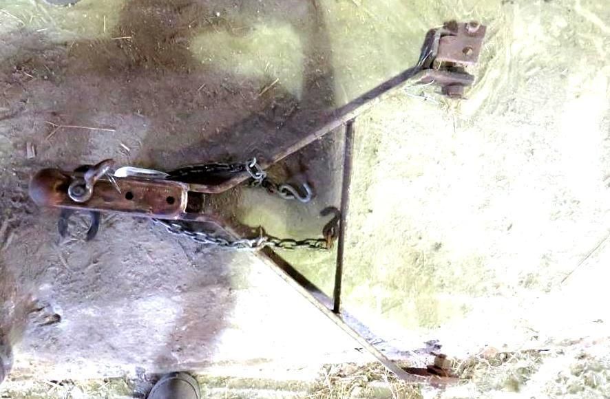 Handmade metal trap on a light-colored surface with a chain and wooden component.