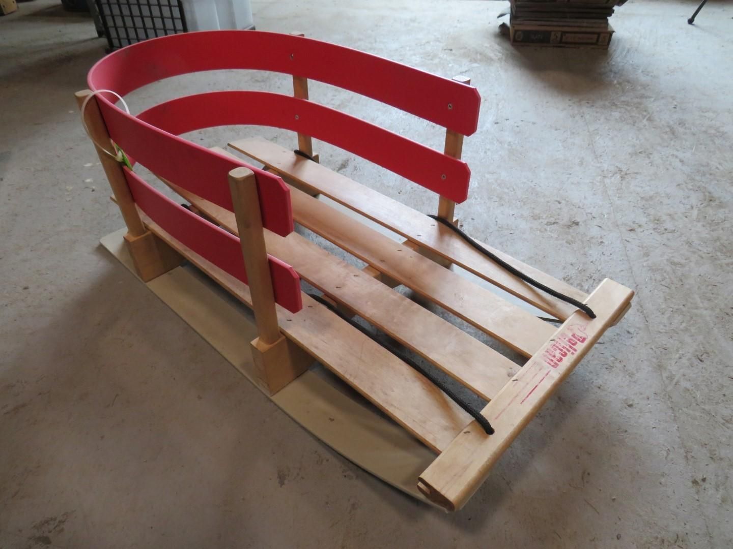 Red and wood sled with curved side rails and black runners, on a light brown base, indoors.
