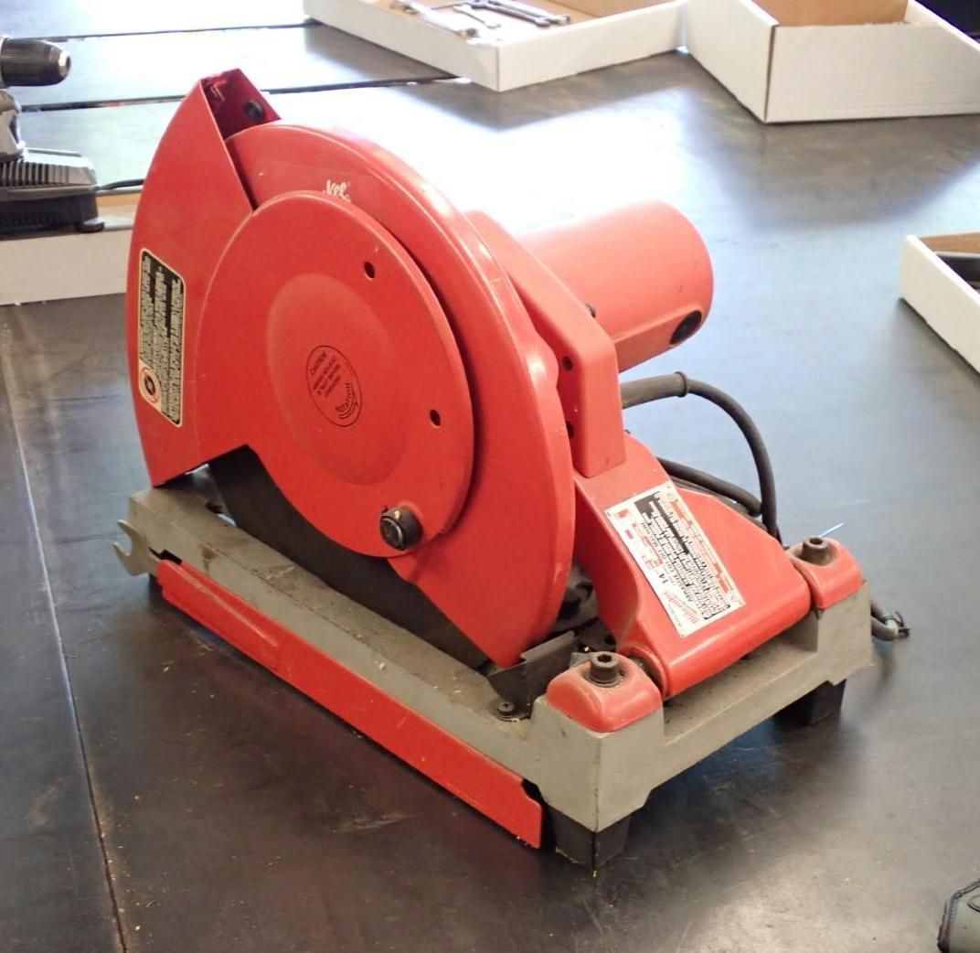 Red and gray metal chop saw on a work surface, ready for cutting.