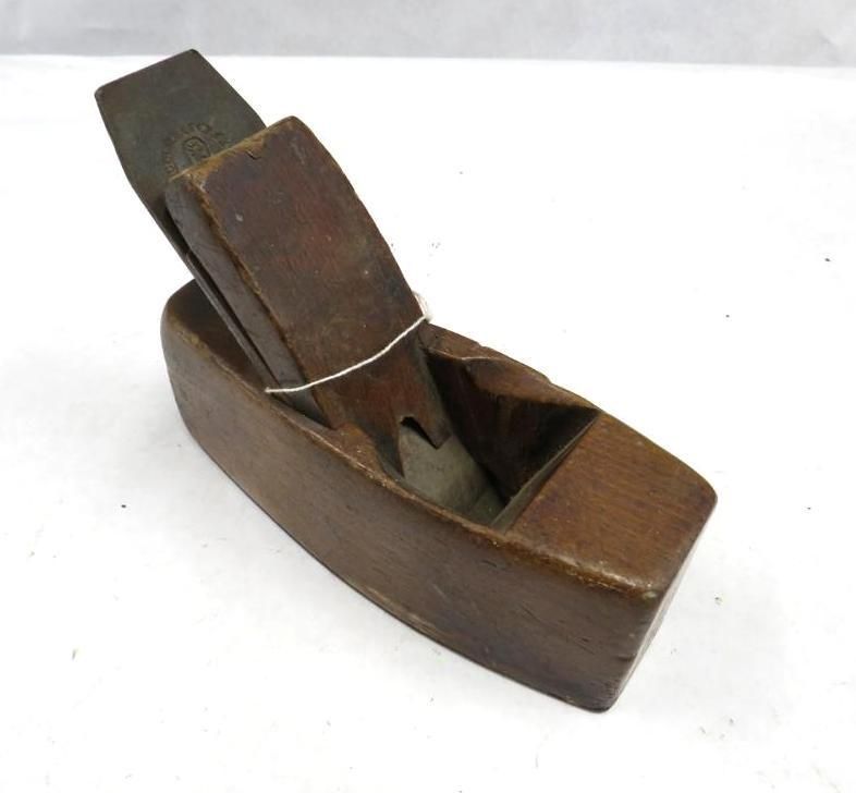 Wooden block plane, dark brown with a blade, sitting on a white surface.