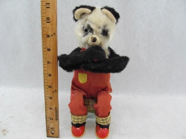 Panda doll wearing orange overalls and black arms, with a wooden ruler.