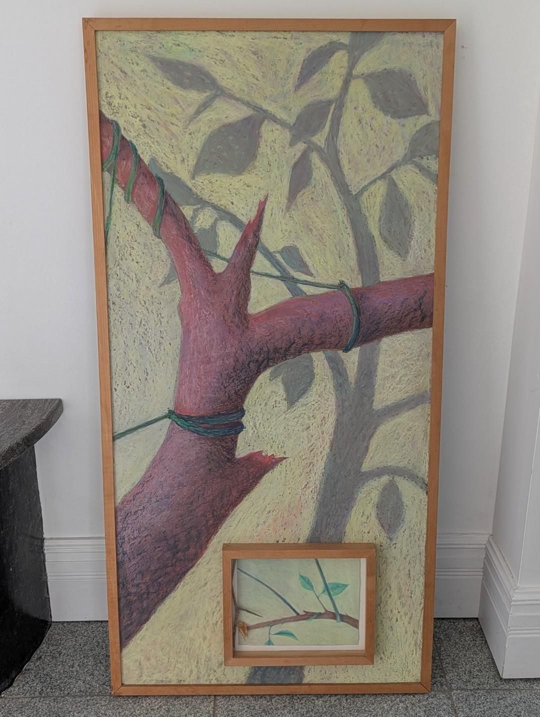 Framed tree branch painting leaning against a white wall, with a small framed landscape inset at the bottom.