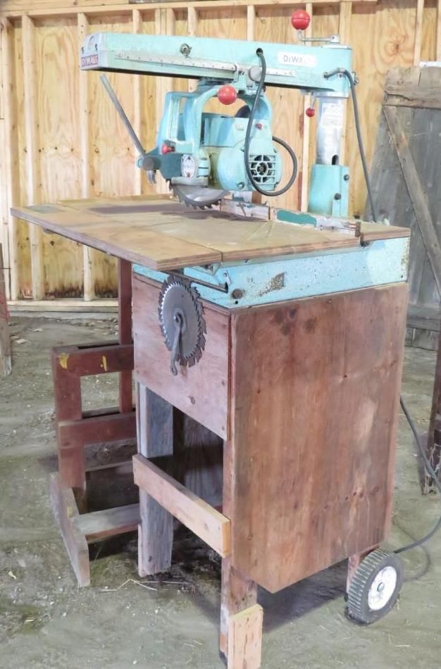 A vintage teal and brown radial arm saw on a wooden stand with a wooden work surface.