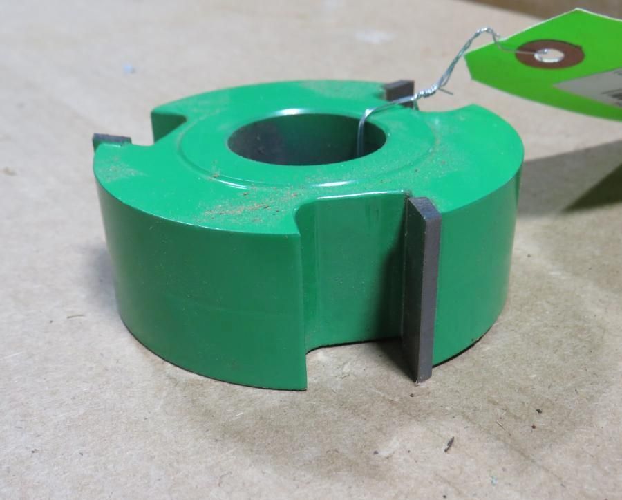 Green router bit with three blades, resting on a surface.