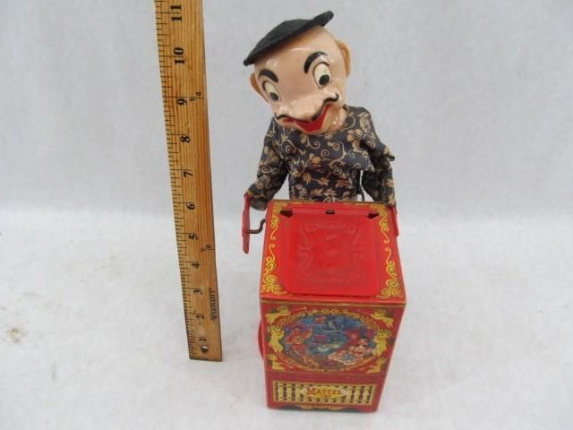 Wind-up toy with a grinning figure wearing a beret, operating a red music box. A ruler is next to it.