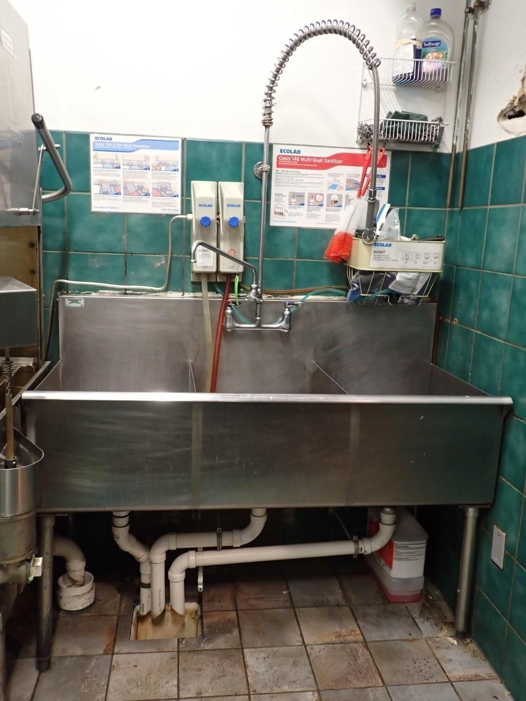 Stainless steel commercial kitchen sink with a high arc faucet, green tiled wall, and plumbing.