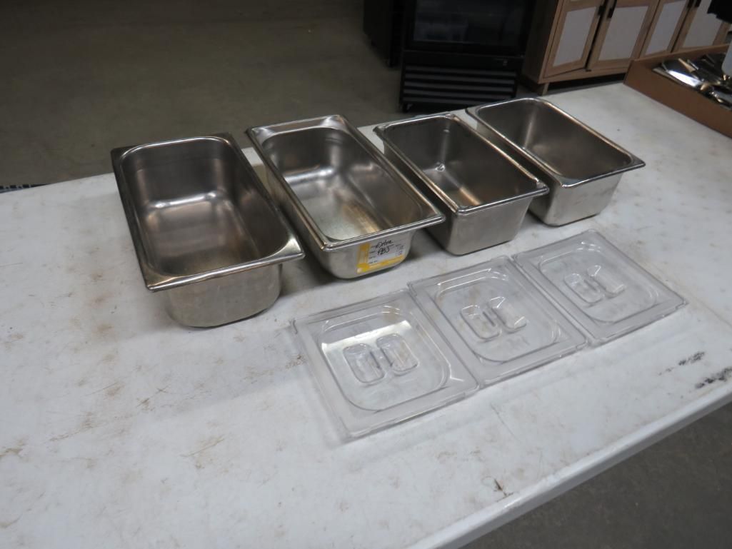 Four stainless steel food pans and three clear plastic lids on a white surface.