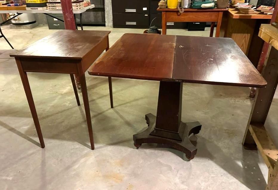 Two antique wooden tables, one rectangular, one square, on a concrete floor in a room.