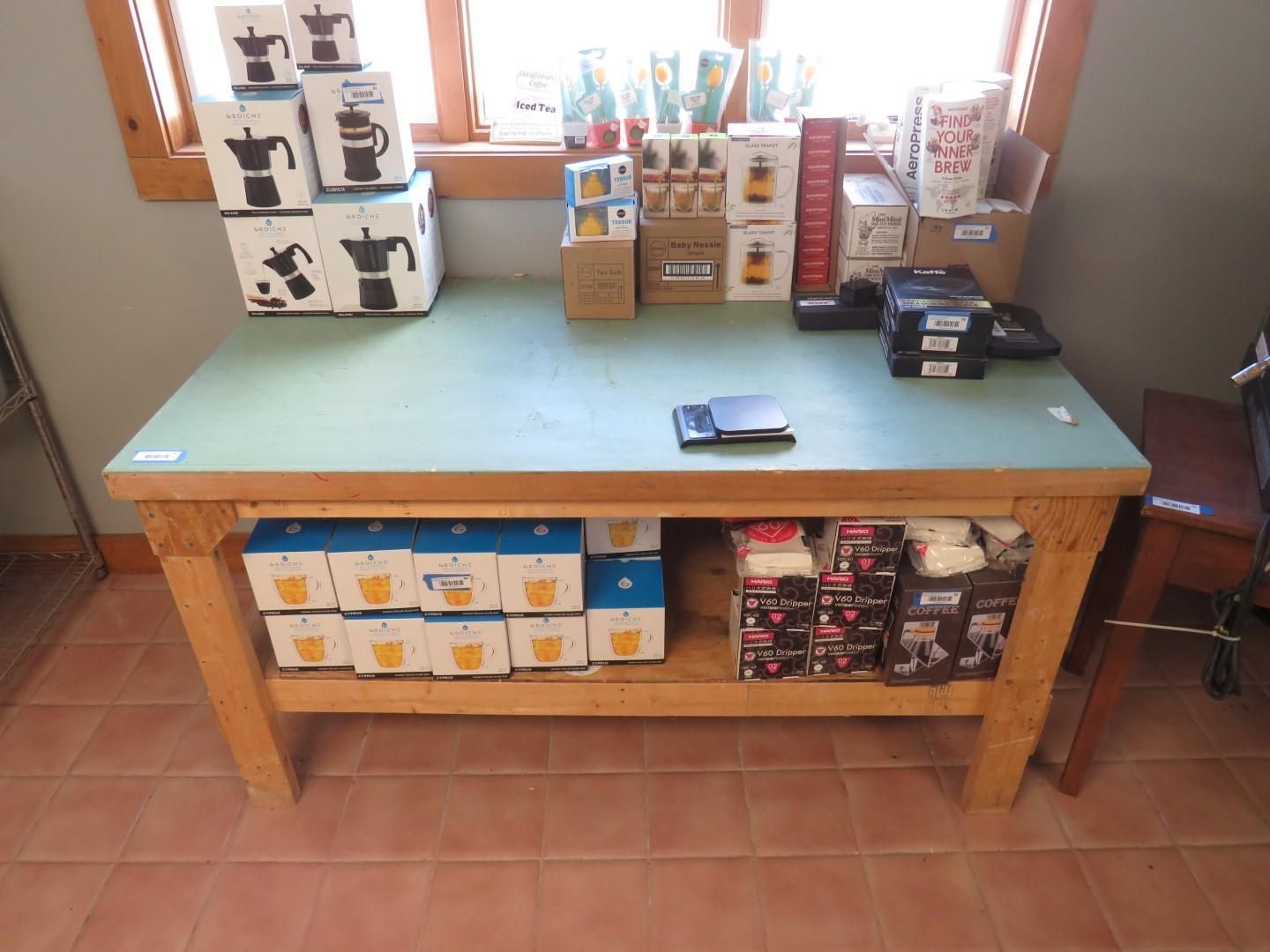 Wooden table displaying coffee makers, cups, and accessories near a window.