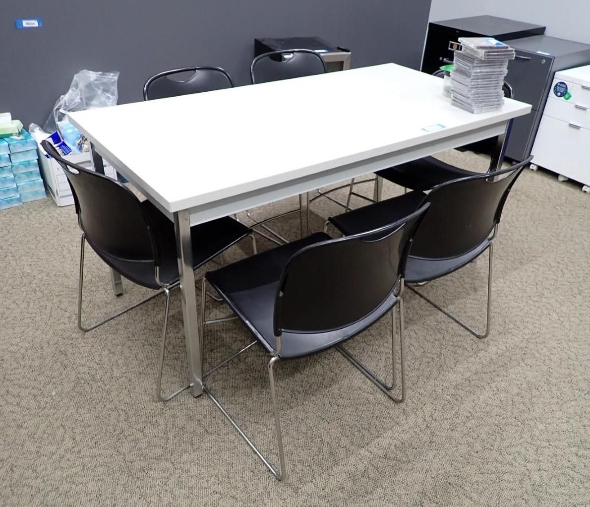 White rectangular table with six black chairs, in a room with a patterned carpet.